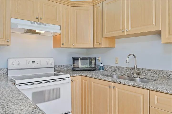Kitchen featuring white range with electric cooktop, light stone counters, light wood finish cabinets, and black microwave