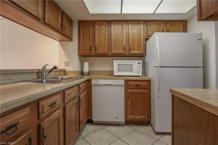Kitchen featuring brown cabinets, white appliances, light countertops, and light tile patterned flooring