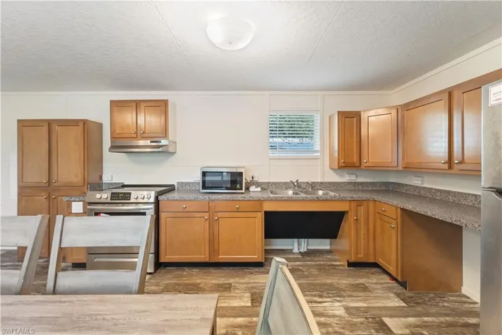 Kitchen with stainless steel appliances, under cabinet range hood, a sink, dark wood-type flooring, and a textured ceiling