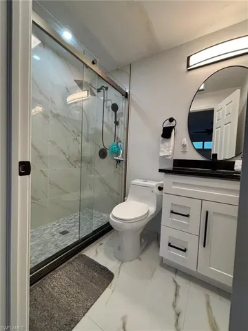 Bathroom with vanity, a marble finish shower, and light marble finish floors