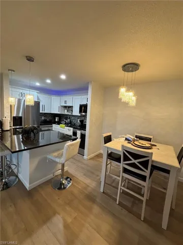 Kitchen with a kitchen bar, white cabinetry, decorative light fixtures, dark stone countertops, and appliances with stainless steel finishes