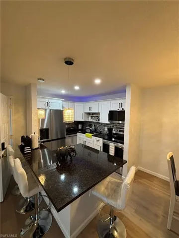 Kitchen with a breakfast bar area, dark stone counters, white cabinets, stainless steel appliances, and recessed lighting