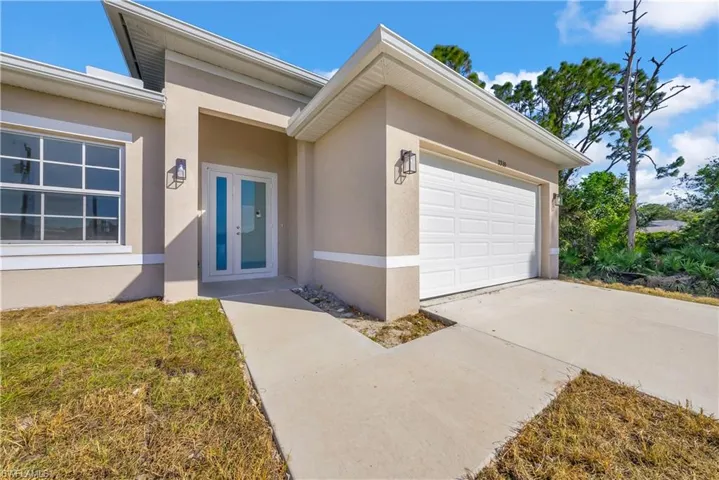 Doorway to property featuring an attached garage, stucco siding, driveway, and a yard