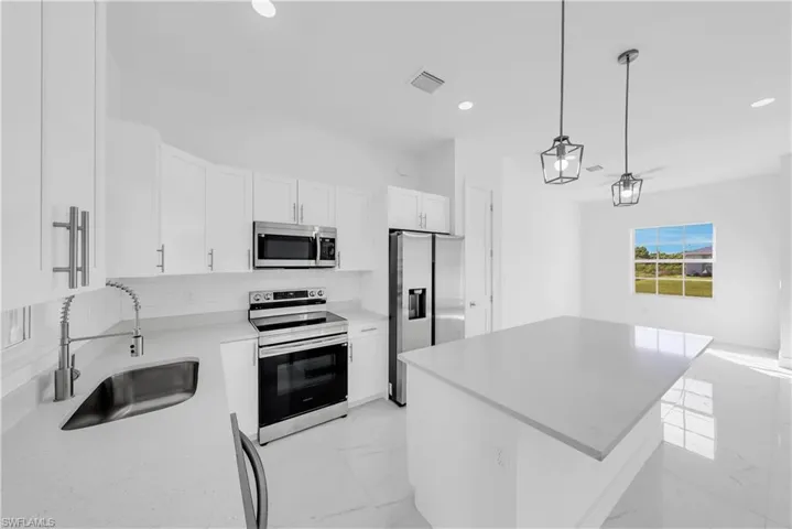 Kitchen featuring stainless steel appliances, a center island, light marble finish flooring, white cabinetry, and decorative backsplash