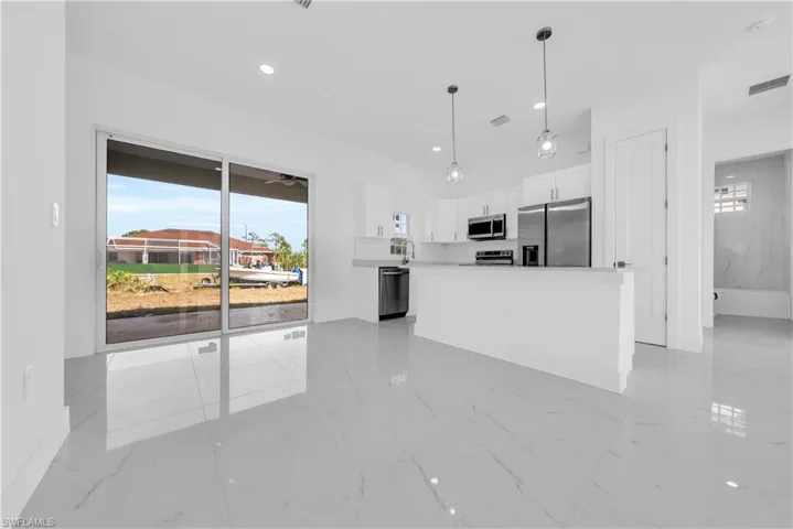 Kitchen featuring healthy amount of natural light, stainless steel appliances, white cabinets, and decorative light fixtures