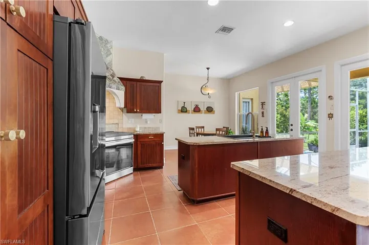 Kitchen featuring decorative columns, a kitchen island with sink, backsplash, appliances with stainless steel finishes, and recessed lighting