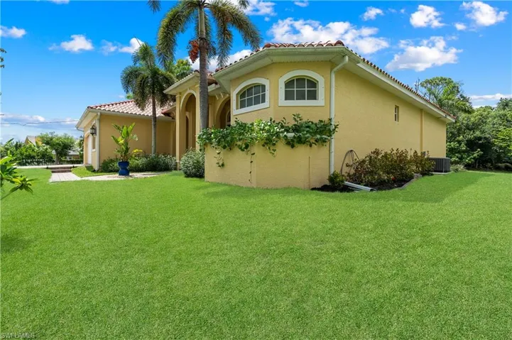 Back of house with a lawn, a tile roof, stucco siding, and a lanai