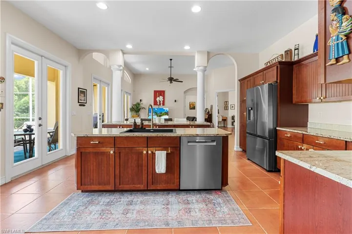 Kitchen with an island with sink, stainless steel fridge, light tile patterned floors, pendant lighting, and tasteful backsplash