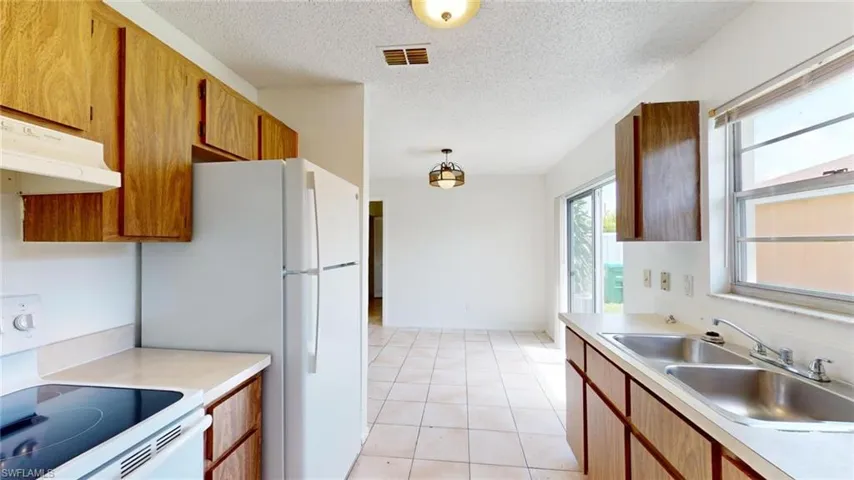 Kitchen with white electric range, light tile patterned floors, sink, and a textured ceiling