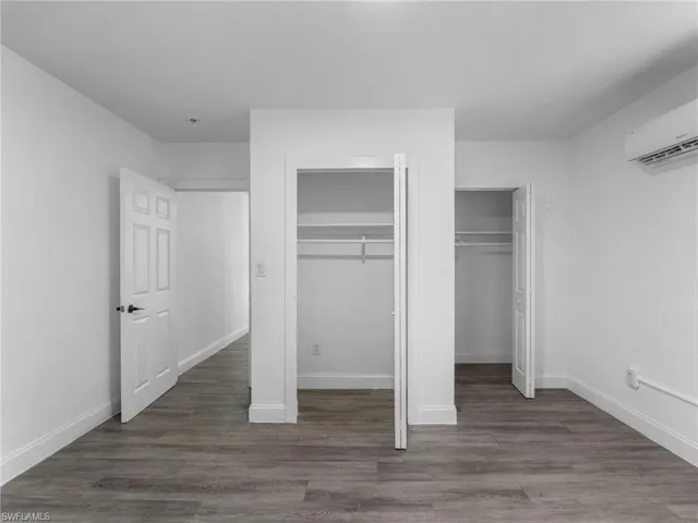 Unfurnished bedroom featuring multiple closets, dark wood-type flooring, and a wall mounted AC