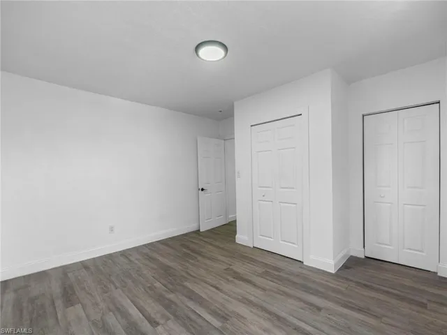 Unfurnished bedroom featuring dark wood-style flooring and two closets
