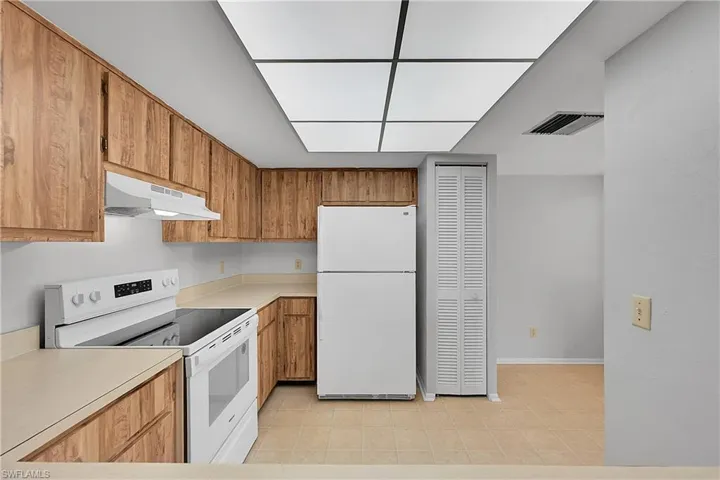 Kitchen with white appliances, light countertops, brown cabinetry, and under cabinet range hood