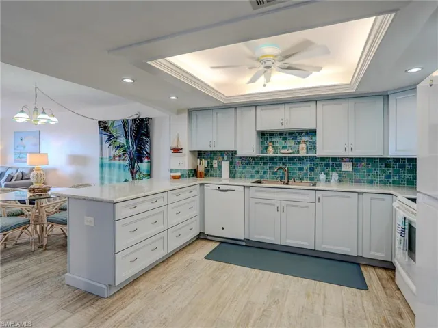 Kitchen featuring sink, white appliances, a raised ceiling, and kitchen peninsula