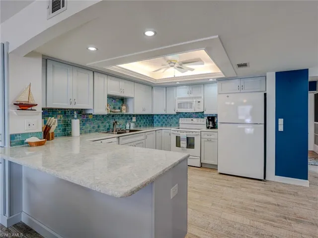 Kitchen with sink, kitchen peninsula, a raised ceiling, white appliances, and light hardwood / wood-style floors