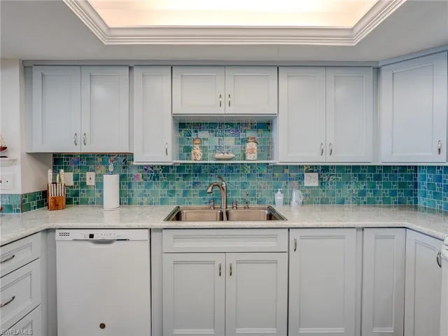 Kitchen featuring sink, dishwasher, white cabinetry, backsplash, and ornamental molding