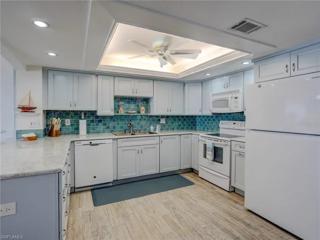 Kitchen featuring a raised ceiling, sink, white appliances, and light hardwood / wood-style flooring
