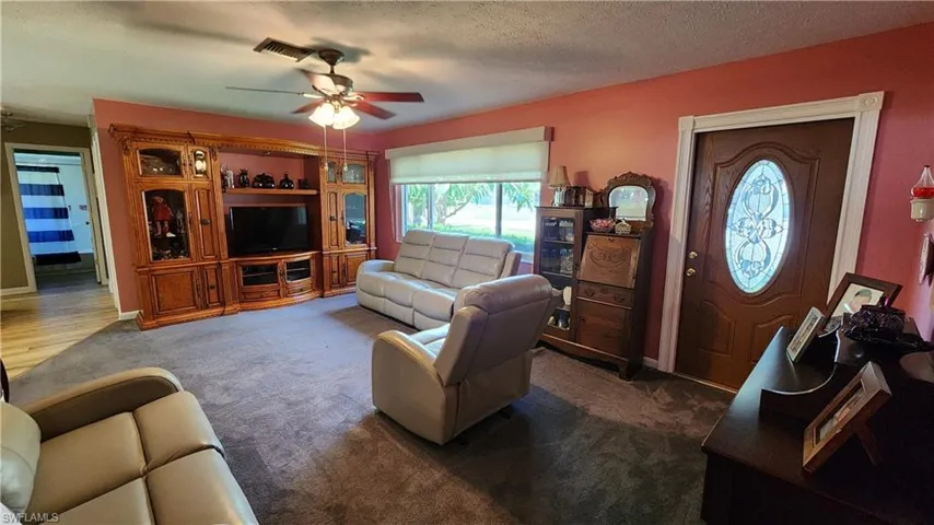Carpeted living room featuring ceiling fan and a textured ceiling
