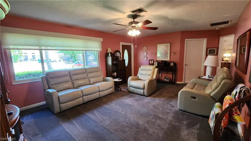 Living room with dark carpet, ceiling fan, and a textured ceiling