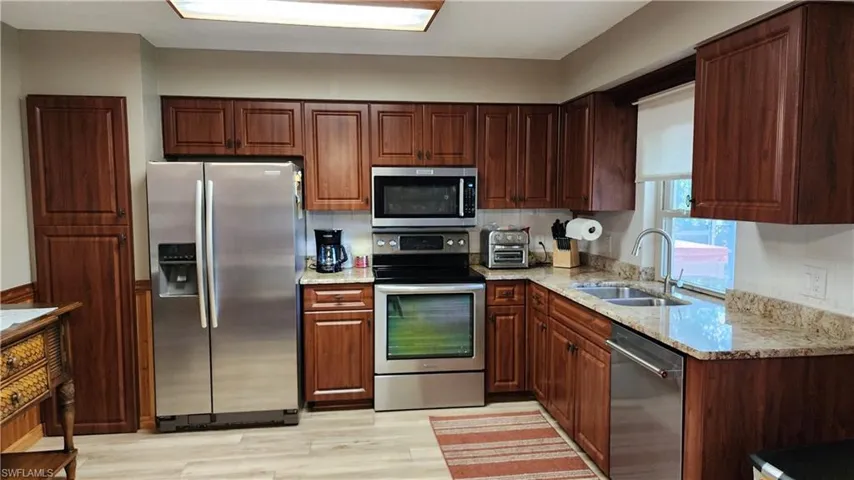 Kitchen with light stone countertops, light hardwood / wood-style floors, tasteful backsplash, sink, and appliances with stainless steel finishes