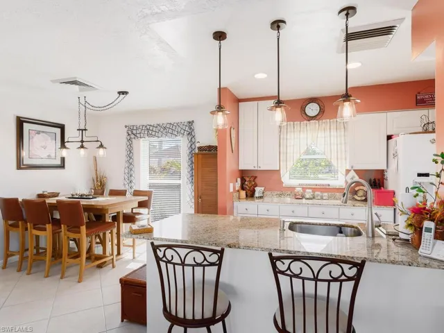 Kitchen with a sink, white cabinets, decorative light fixtures, and white fridge with ice dispenser