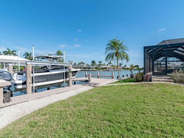 Dock area featuring boat lift, a lawn, a water view, and glass enclosure