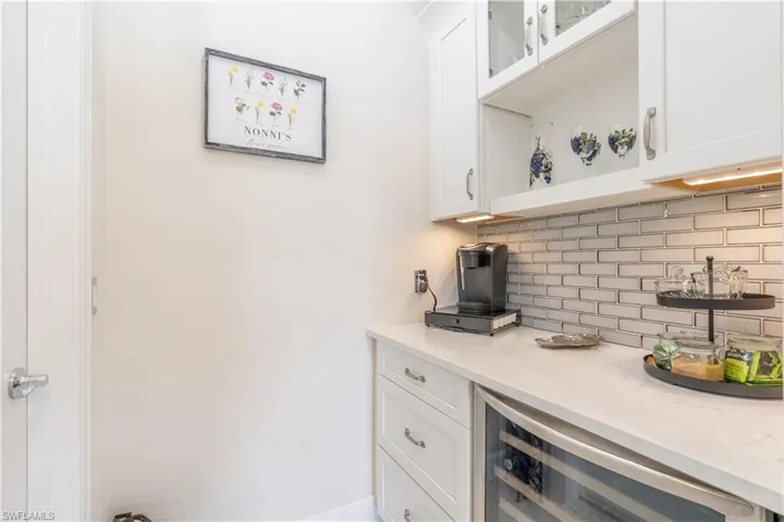 Bar with decorative backsplash, white cabinetry, wine cooler, and light stone counters
