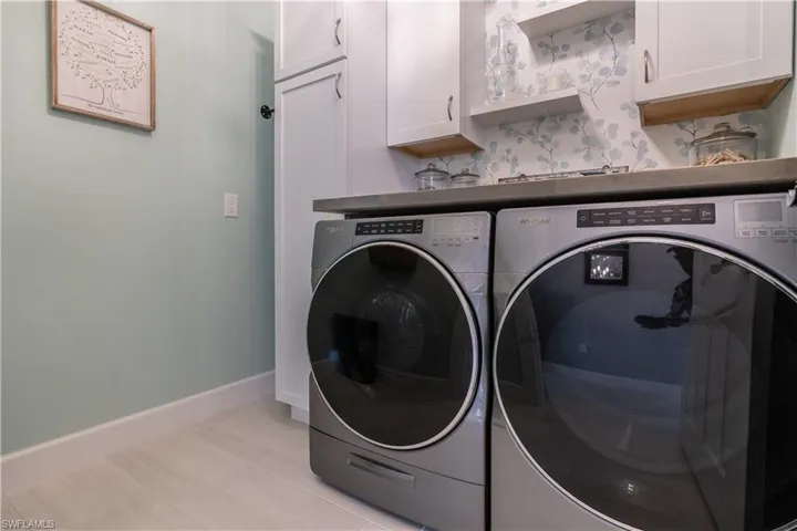 Laundry room with light tile patterned flooring, cabinets, and washing machine and clothes dryer