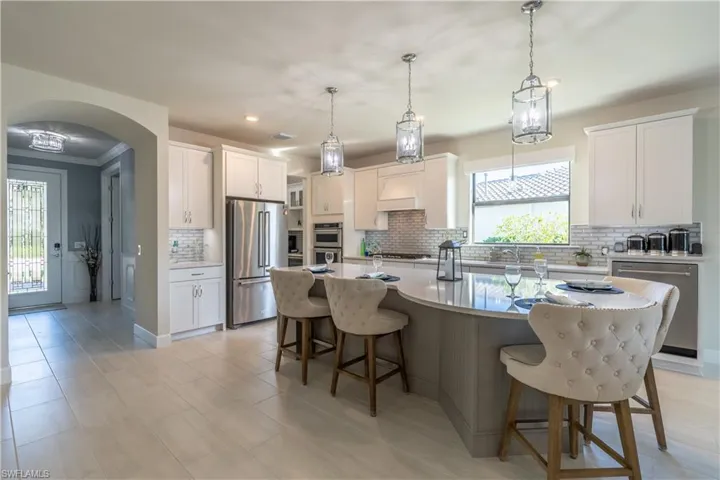 Kitchen featuring tasteful backsplash, stainless steel appliances, white cabinetry, and a kitchen island with sink
