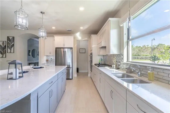 Kitchen featuring appliances with stainless steel finishes, tasteful backsplash, sink, white cabinetry, and hanging light fixtures