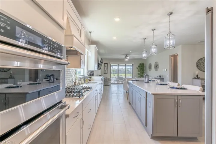 Kitchen featuring appliances with stainless steel finishes, white cabinetry, hanging light fixtures, and an island with sink