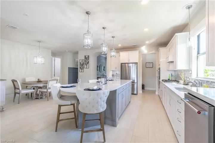 Kitchen featuring a large island with sink, hanging light fixtures, white cabinets, and stainless steel appliances