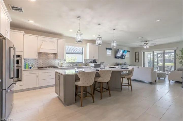 Kitchen featuring high end refrigerator, white cabinetry, a center island with sink, and decorative light fixtures