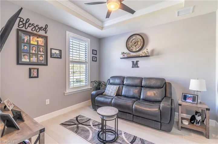 Tiled living room with a tray ceiling, crown molding, and ceiling fan