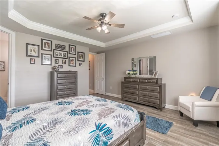 Bedroom with ceiling fan, light wood-type flooring, ornamental molding, and a tray ceiling