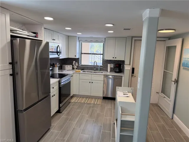 Kitchen featuring stainless steel appliances, white cabinets, wood tiled floors, decorative backsplash, and recessed lighting