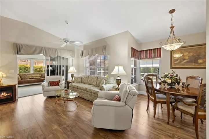 Living area with a ceiling fan, vaulted ceiling, wood finished floors, and a lit fireplace