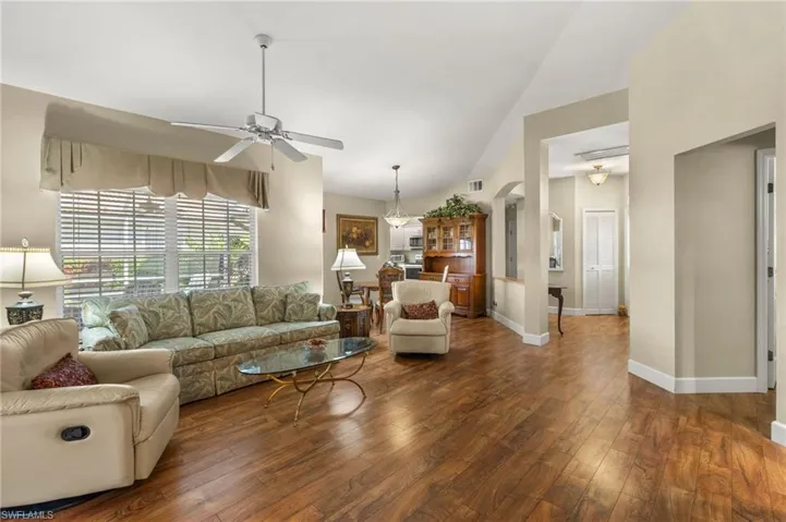 Living room with dark wood-type flooring, baseboards, lofted ceiling, arched walkways, and a ceiling fan