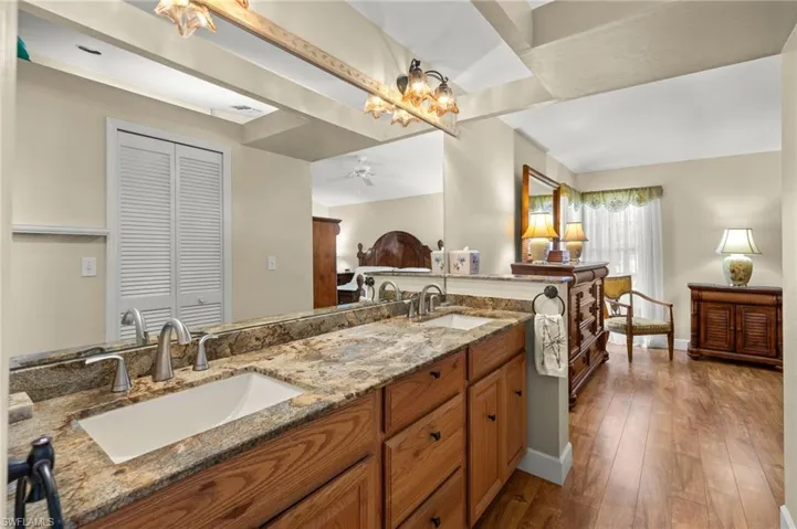 Full bath with double vanity, ceiling fan with notable chandelier, hardwood / wood-style floors, and a sink