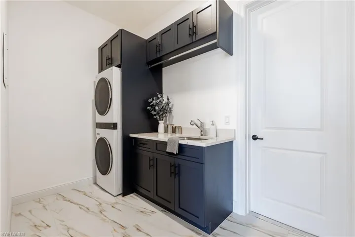Laundry area featuring cabinet space, light marble finish floors, and stacked washer / dryer