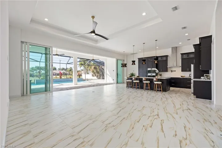 Living area with a sunroom, a raised ceiling, light marble finish flooring, a ceiling fan, and recessed lighting