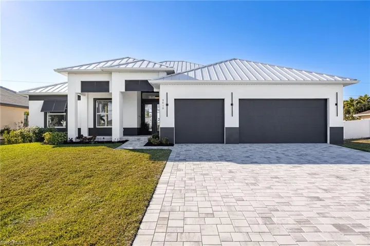 View of front of house with a metal roof, a standing seam roof, a front yard, decorative driveway, and a garage