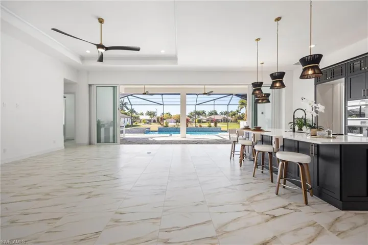 Kitchen with a sunroom, light marble finish floors, dark cabinetry, a breakfast bar, and open floor plan