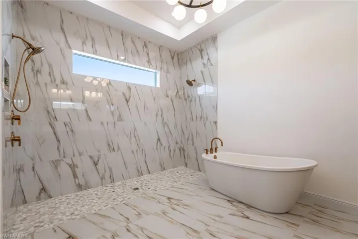 Bathroom featuring a marble finish shower, a soaking tub, a chandelier, and marble tiled flooring