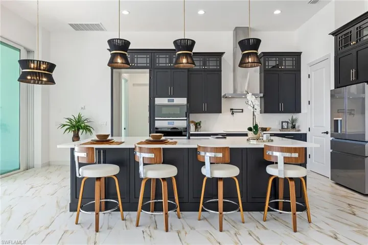 Kitchen with dark cabinets, appliances with stainless steel finishes, a kitchen breakfast bar, a large island with sink, and glass insert cabinets