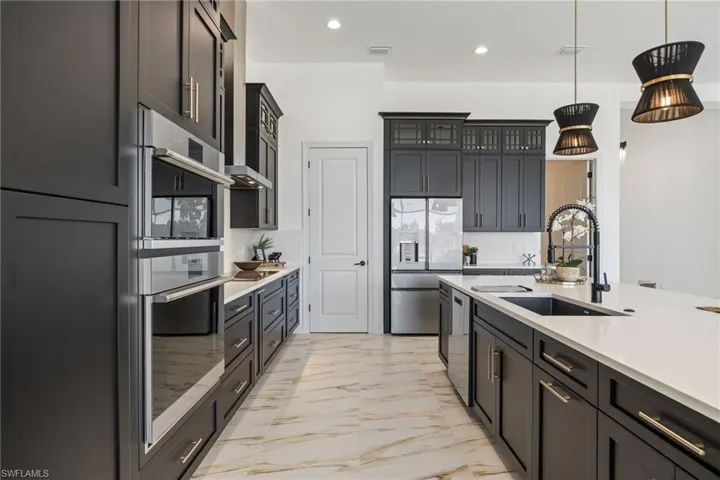 Kitchen with appliances with stainless steel finishes, recessed lighting, light marble finish floors, pendant lighting, and light stone counters