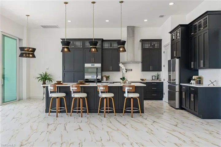 Kitchen featuring a breakfast bar area, decorative light fixtures, a large island, appliances with stainless steel finishes, and light marble finish flooring