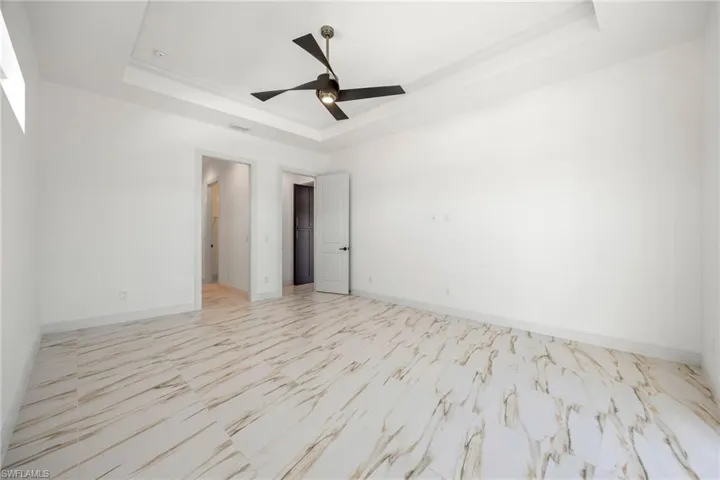 Unfurnished room with a raised ceiling, light marble finish flooring, and ceiling fan