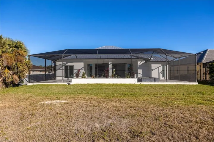 Rear view of property featuring a sunroom, a lanai, a lawn, and a patio