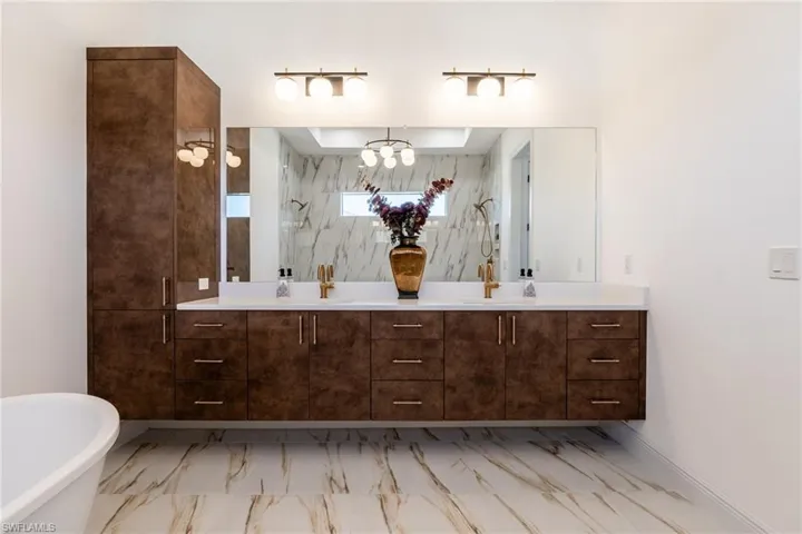 Full bath featuring double vanity, a freestanding bath, light marble finish flooring, and a marble finish shower
