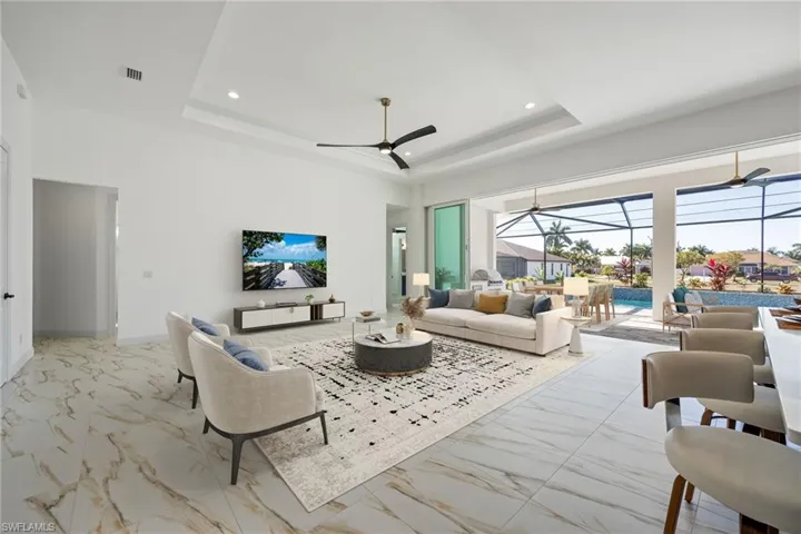 AI Staged photo.  Living room featuring a sunroom, a tray ceiling, recessed lighting, and light marble finish flooring